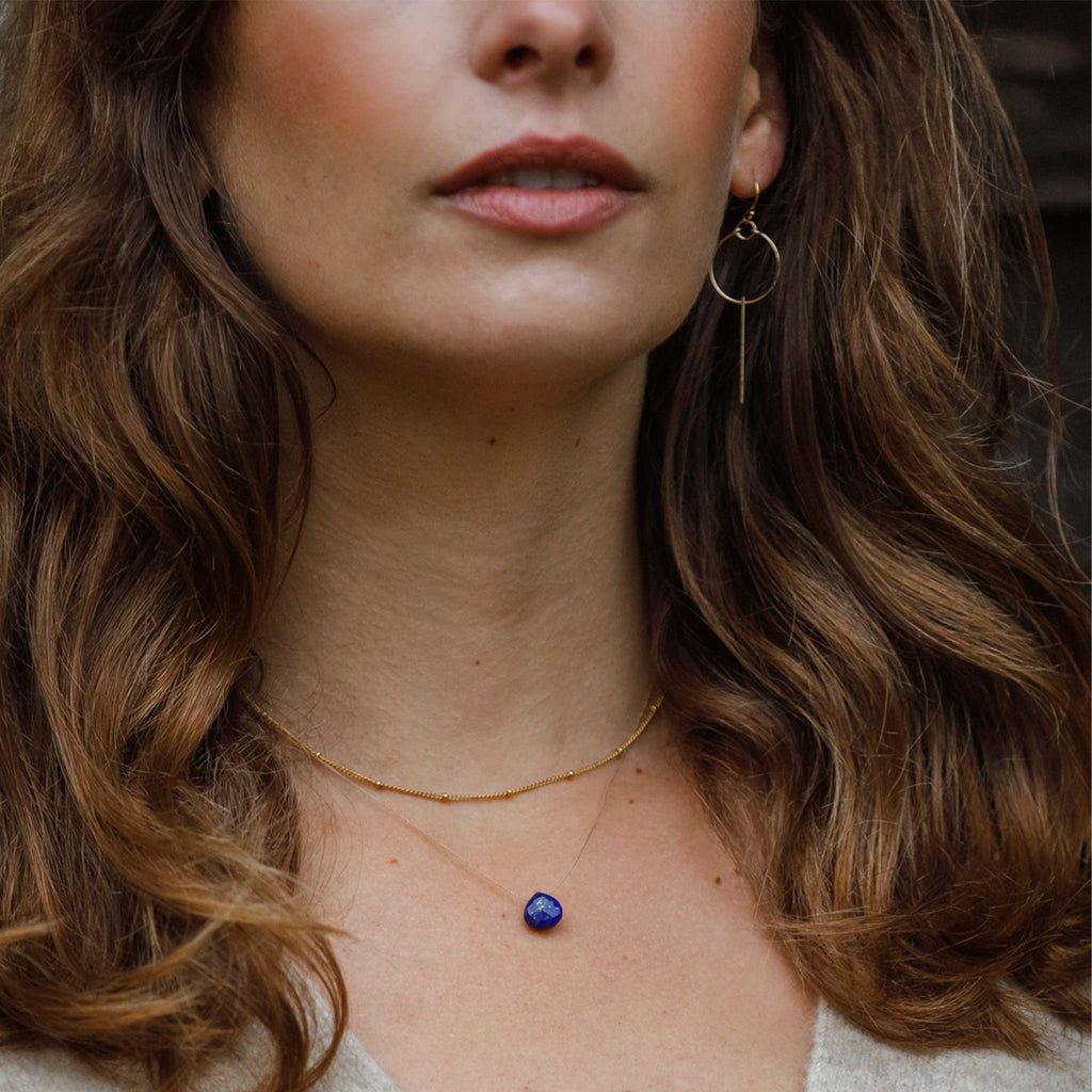 A Lapis Lazuli gemstone in a deep, navy blue with gold flecks is strung on a fine cord, creating a minimal and modern gemstone necklace. Styled here in a layered look with the Satellite gold fill layering chain necklace.