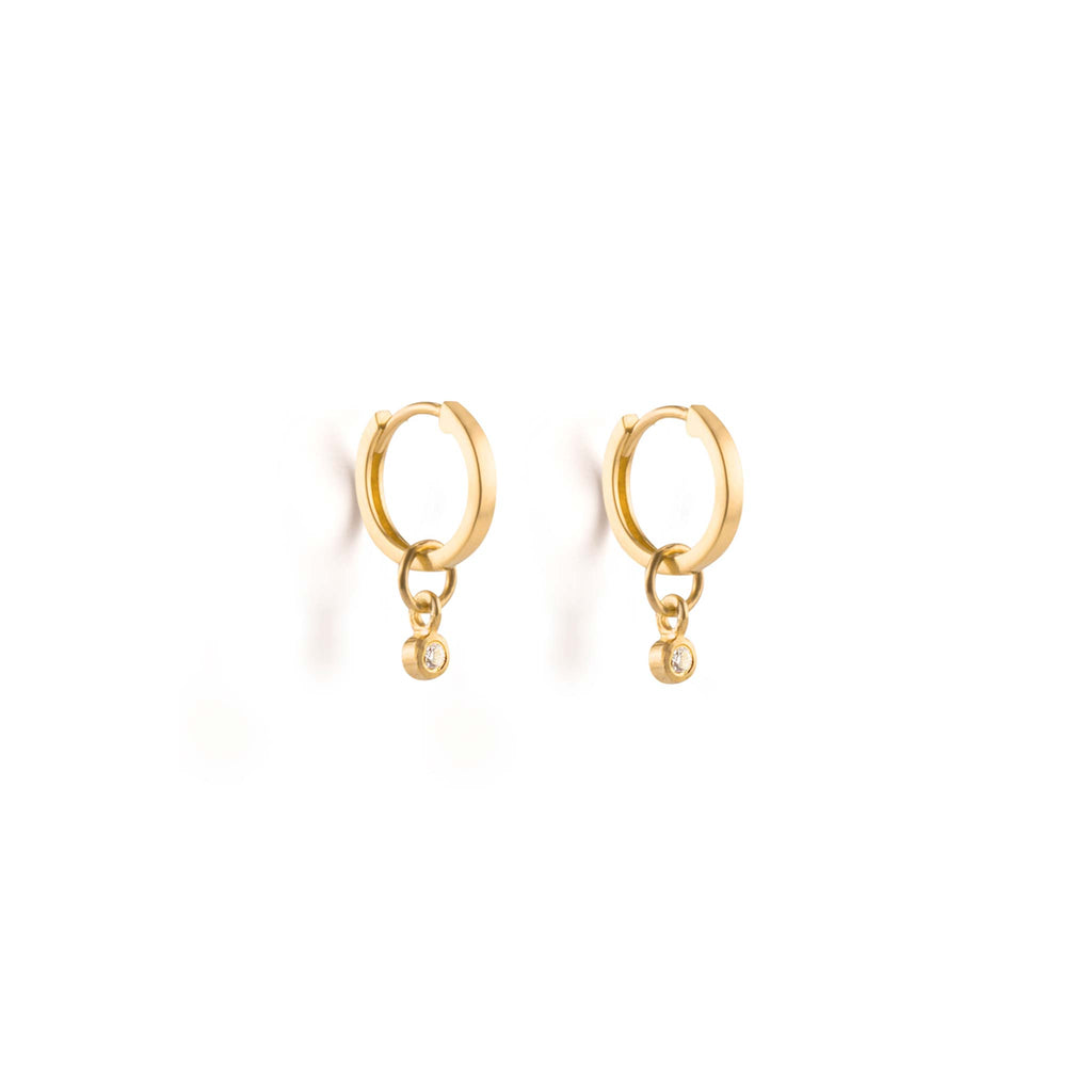 A pair of huggie hoop earrings feature a diamond charm. Made with recycled 9k yellow gold, these hoop earrings add a sparkle to any ear stack. Designed with sustainability in mind in our Devon studio, and handcrafted with recycled gold and lab created diamonds by our Wanderlust Life Global Artisan Partners.