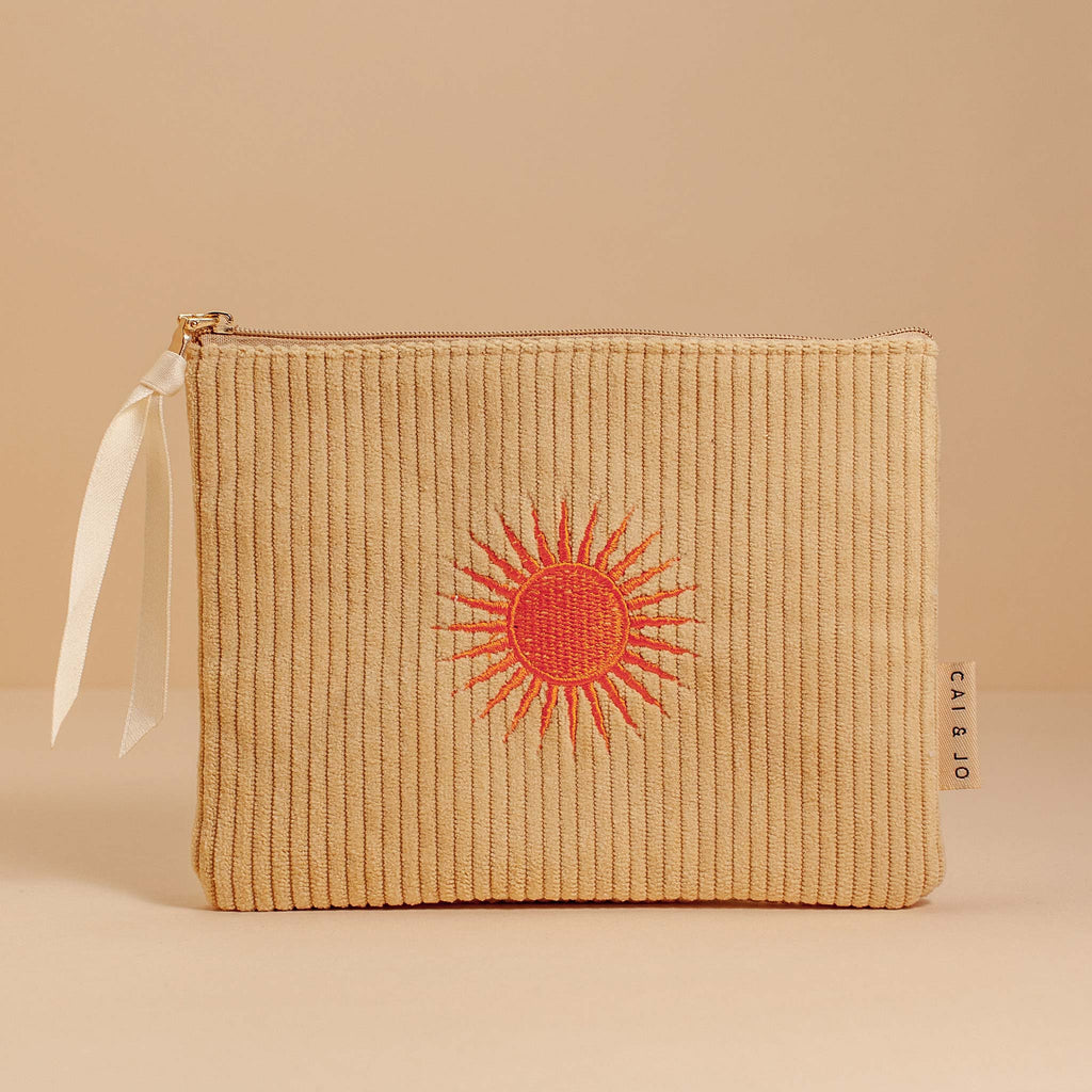 A flat corduroy pouch in a pale ochre colour, featuring an embroidered orange sun motif. 