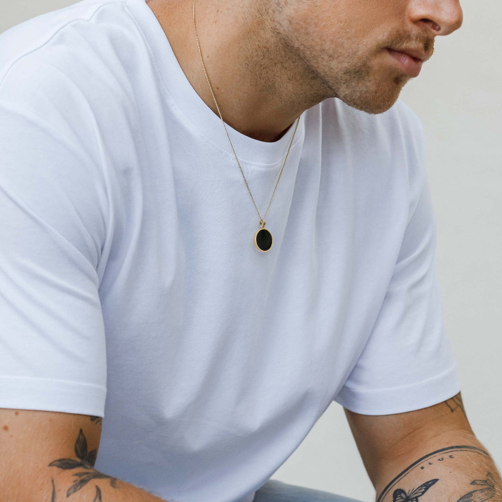 Male model wears Black Onyx Porthole Necklace on Celine Curb Chain. A long, statement necklace with a circular pendant. A Black Onyx gemstone slice is framed around a circle of brushed gold. Unisex jewellery designed by Wanderlust Life.