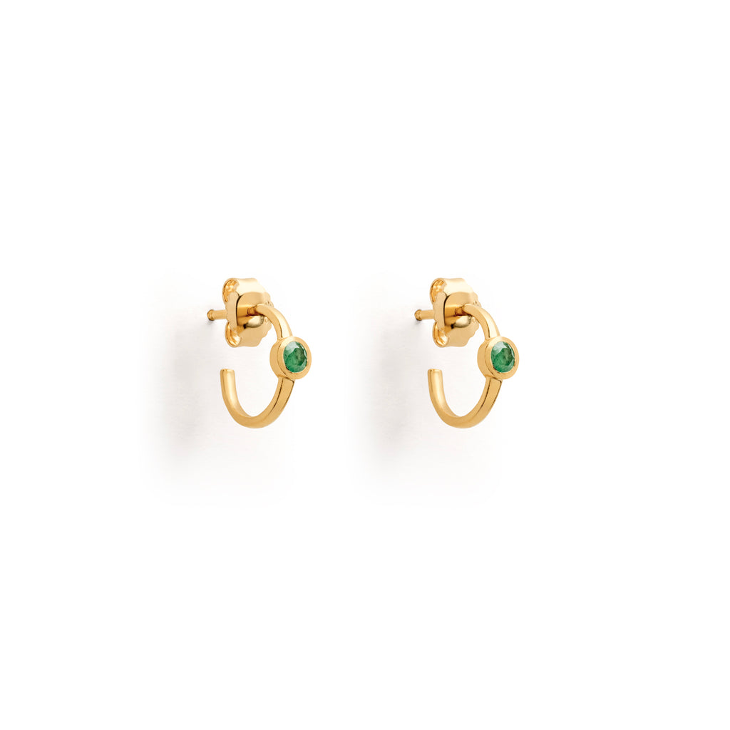 Emerald Astrea Hoop Earrings feature a green emerald semi-precious gemstone on the surface of these gold hoops. three-quarter C-hoop earrings made with 14k gold vermeil. Minimal hoop earrings which effortlessly style into any ear stack. Perfect for everyday styling. Designed in Devon and handcrafted by our Global Artisan Partners.