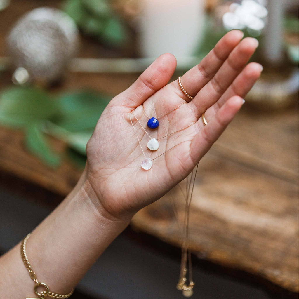 Our signature Fine Cord Necklaces in Lapis Lazuli, Mother of Pearl and Rainbow Moonstone is held in a hand.