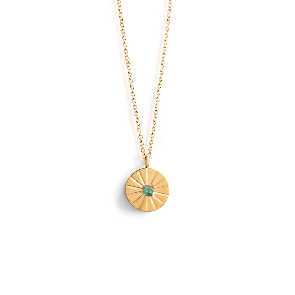Wanderlust Life Emerald May Birthstone Mini Sundial Necklace. Etched beams radiate from a small emerald gemstone in the centre of this gold disc pendant. Adjustable in length, perfect for necklace stack layering. Modern, minimal and meaningful gift. Personalised jewellery. Engrave with free engraving. Designed in Devon, and handcrafted by our Wanderlust Life Global Artisan Partners.