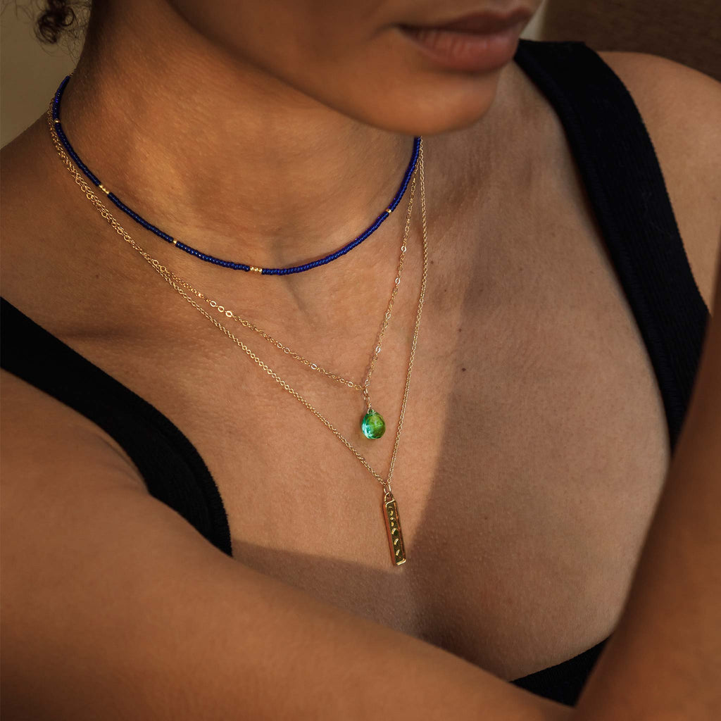 The Morocco Blue Beaded Necklace is a choker style beaded necklace, with an adjustable length. Perfect for layering, this bright blue necklace is styled with a green gemstone necklace and a gold pendant necklace.