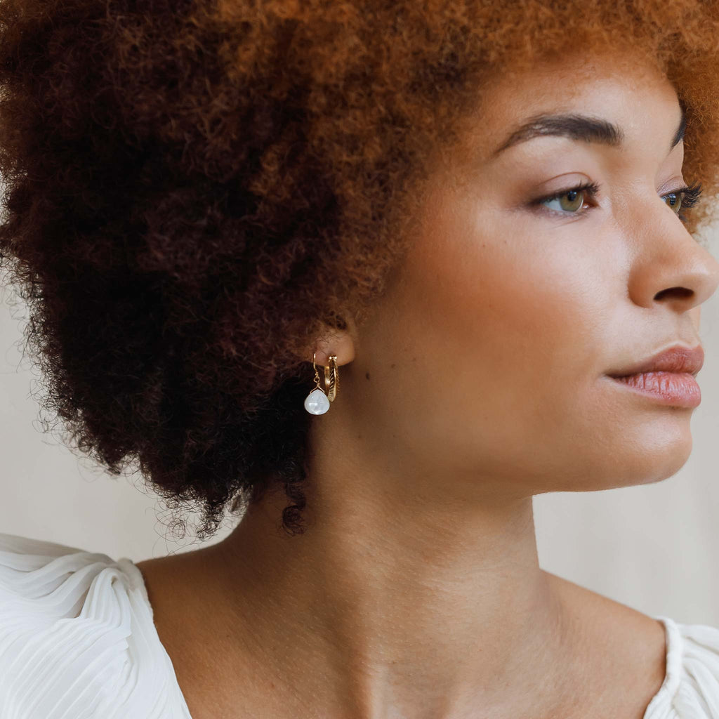 Iridescent mother of pearl gemstone hangs from a minimal gold earwire. These iridescent and pearly drop earrings are styled in an ear stack with classic hoops.