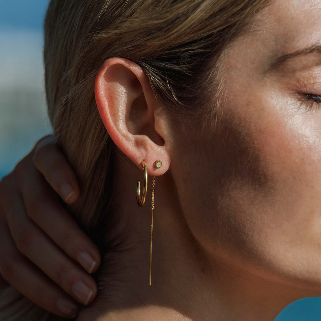 Worn in the first piercing on the lobe, the Opal Volta Earrings feature an opal stud that sits at the front of the lobe, followed by a golden length of chain and a bar which threads through your piercing. Styled in an ear stack with the Medium Silke Hoops.
