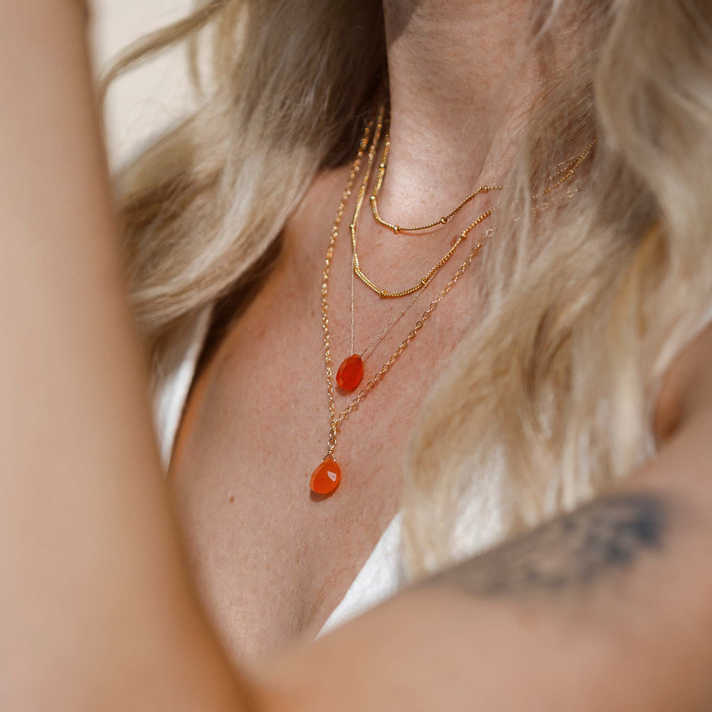 The orange carnelian fine cord necklace features a sunset orange gemstone, floating on a minimal fine cord. Styled with the orange carnelian gemstone pendant necklace and two satellite layering chains.