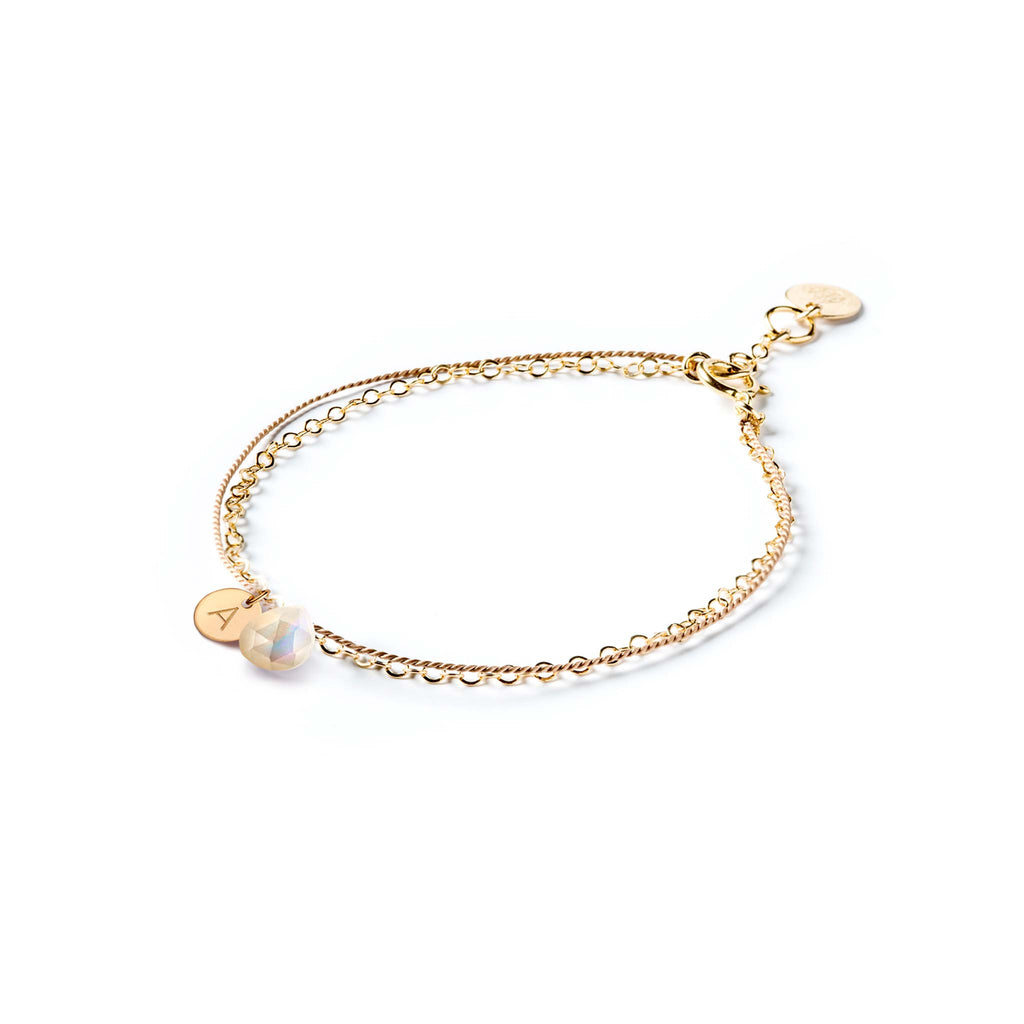 A gold and silk bracelet featuring a mother of pearl stone and an initial charm, hand-stamped with an A.