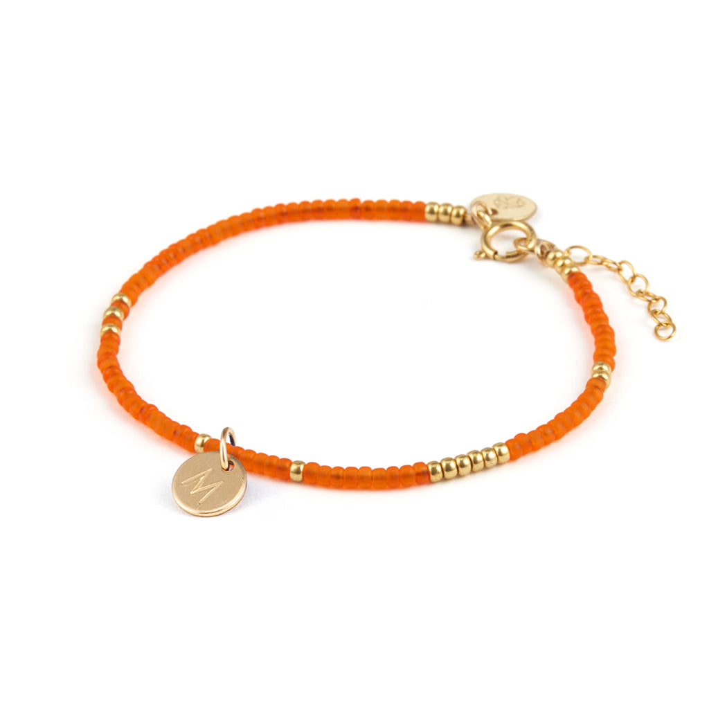 Personalised with a gold fill, initial charm stamped with an M. A bright orange beaded bracelet featuring intervals of gold beads.