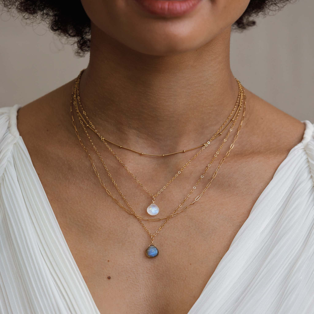 Model wears four necklaces layered together. The Satellite chain is a choker length layering chain, styled with the rainbow moonstone and labradorite pendant necklaces, and the Sylvie necklace, a long paperclip style layering chain. 