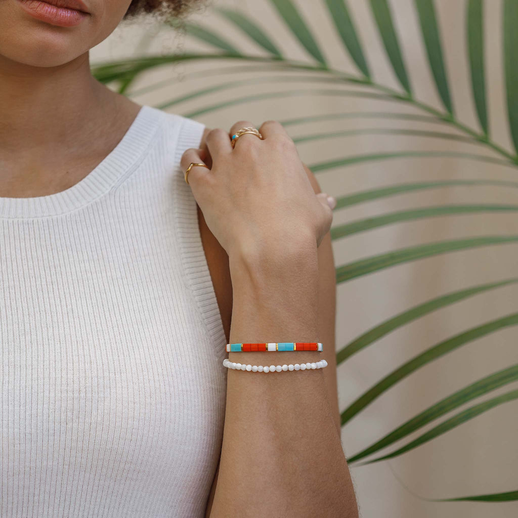 The Safi Layering Bracelet features burn orange, turquoise, gold and white tile beads, strung on elastic for an adjustable and stretchy fit. It's styled here with a beaded mother of pearl gemstone bracelet.