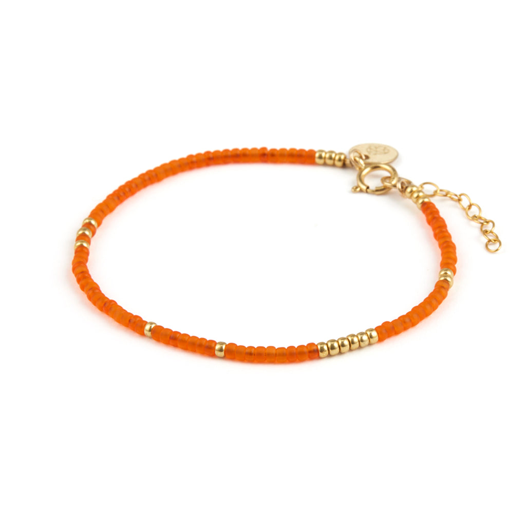 A beaded bright orange bracelet featuring gold beads, an adjuster chain and branded Wanderlust Life Jewellery.