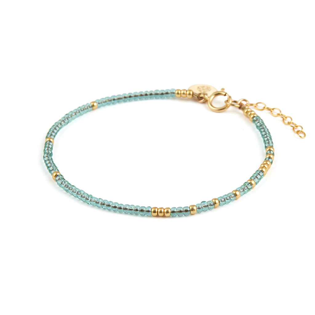A gold and blue beaded bracelet featuring translucent water blue beads, contrasted with gold beads. This bracelet features a length of chain to make it an adjustable size. Designed and handcrafted in Devon.