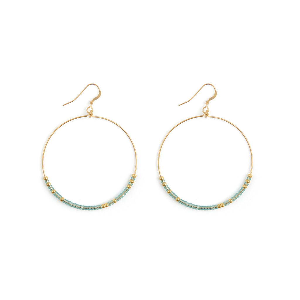 Large hoops drop from ear wire hooks. Made with golf fill, these hoops are decorated with translucent water blue seed beads, contrasted with gold.