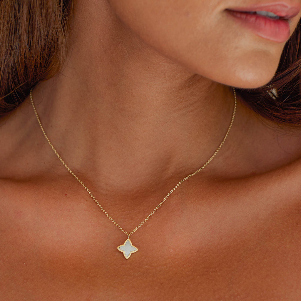 The Mother of Pearl Compass Star Necklace resembles a four-leaf clover and a star inspired by compasses and nautical charts. The pendant frames a slice of mother of pearl gemstone with a gold frame. On an adjustable length chain, this necklace is an everyday icon.