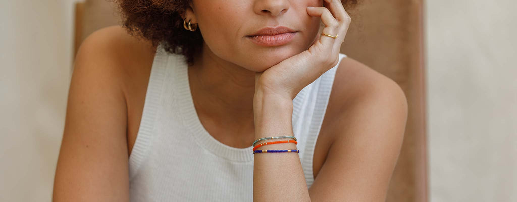Model wears a beaded bracelet stack featuring vibrant orange, water blue and cobalt blue seed bead bracelets.Shop beaded bracelets online at Wanderlust Life Jewellery.