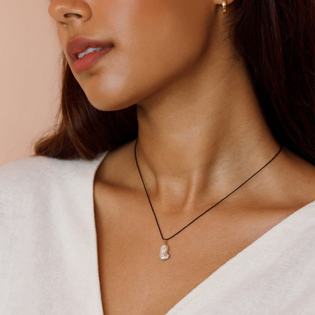 Model wearing a single freshwater “Kiwa” shaped pearl strung on a black silk cord - a striking twist on our signature fine cord necklaces. 