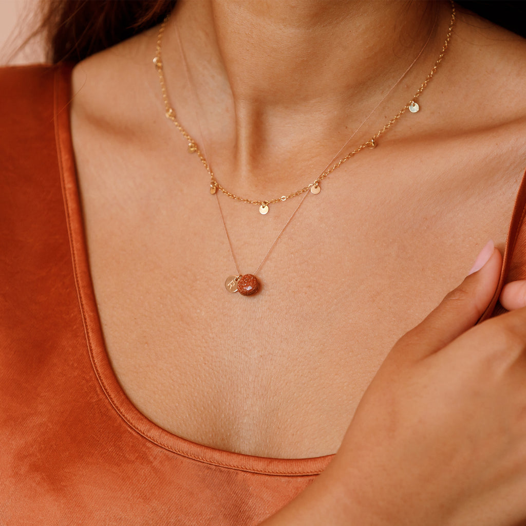 Model wearing a  radiant copper-flecked goldstone gemstone strung on a minimal fine cord necklace. Layered with a gold telltale necklace.