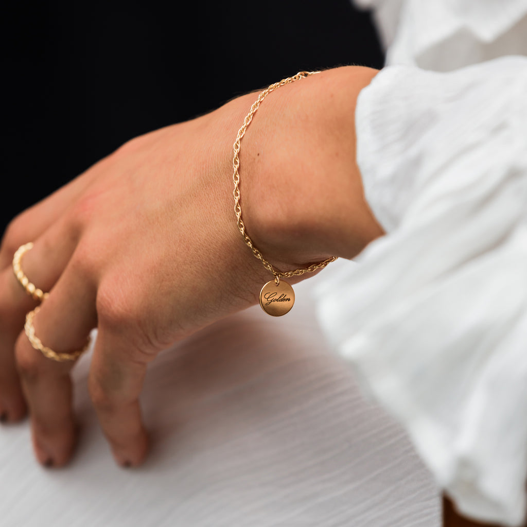 Charged with meaning, an engravable disc with 'golden' in script font slides on an adjustable gold rope chain bracelet.