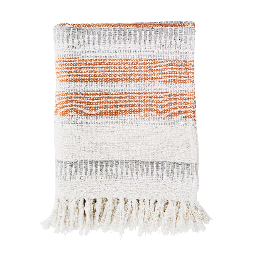 A patterned throw in orange and neutral tones features decorative fringes at the sides. Designed by Madam Stoltz and woven from 100% recycled cotton thread.