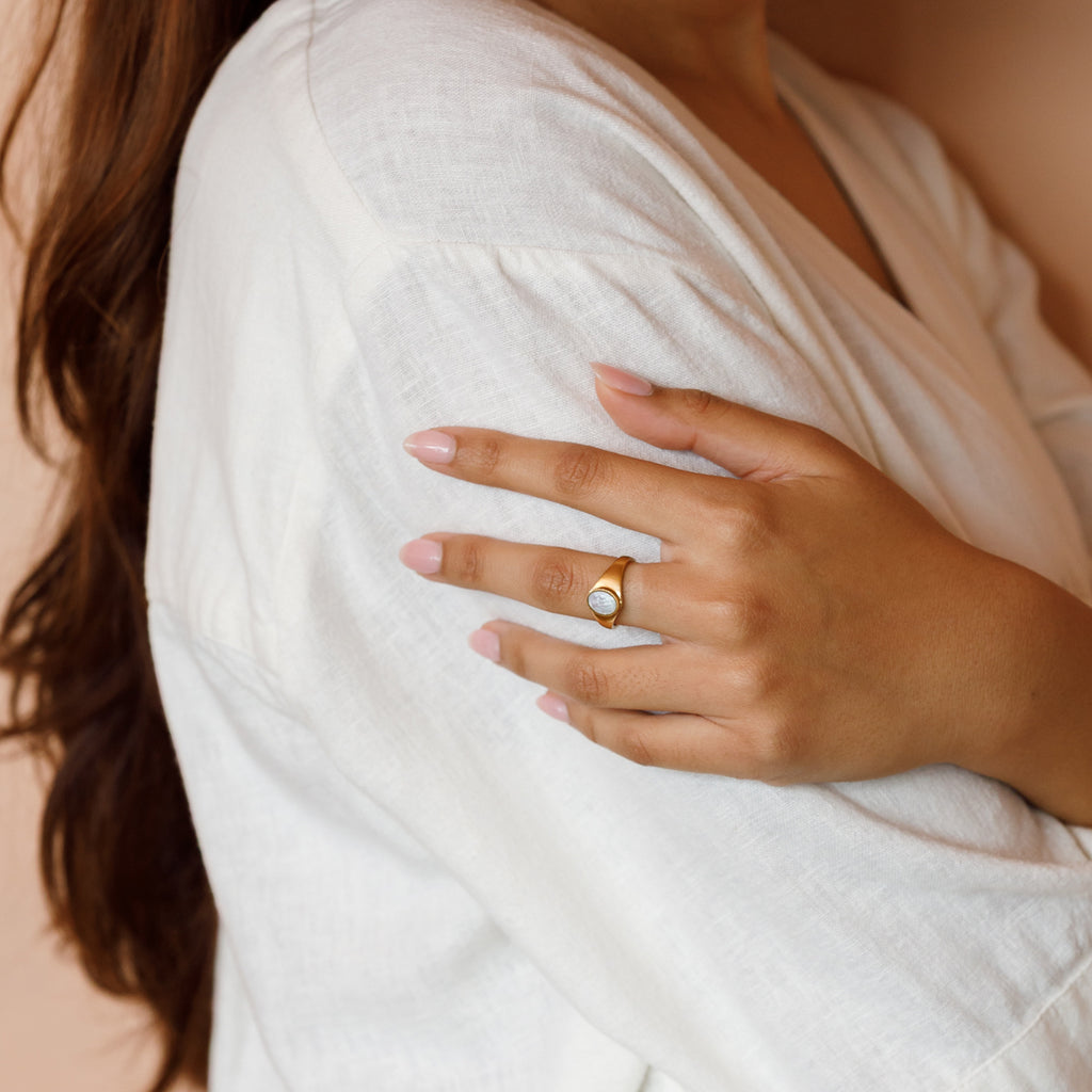 This statement ring features a luminous oval of Mother of Pearl, cradled at the centre of a thick gold band