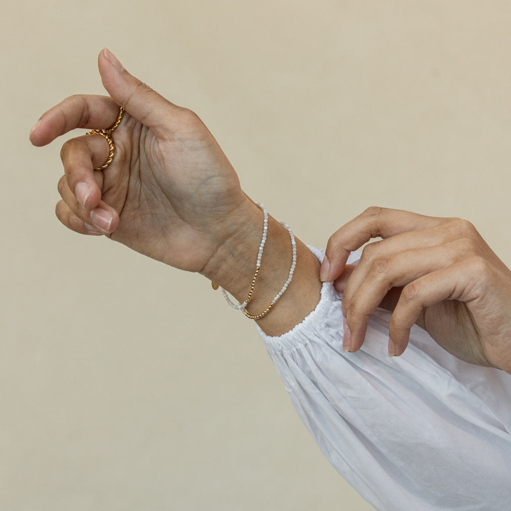 A dainty beaded bracelet with lustrous mother of pearl and gold beads that shimmer like ocean waves under the sun.