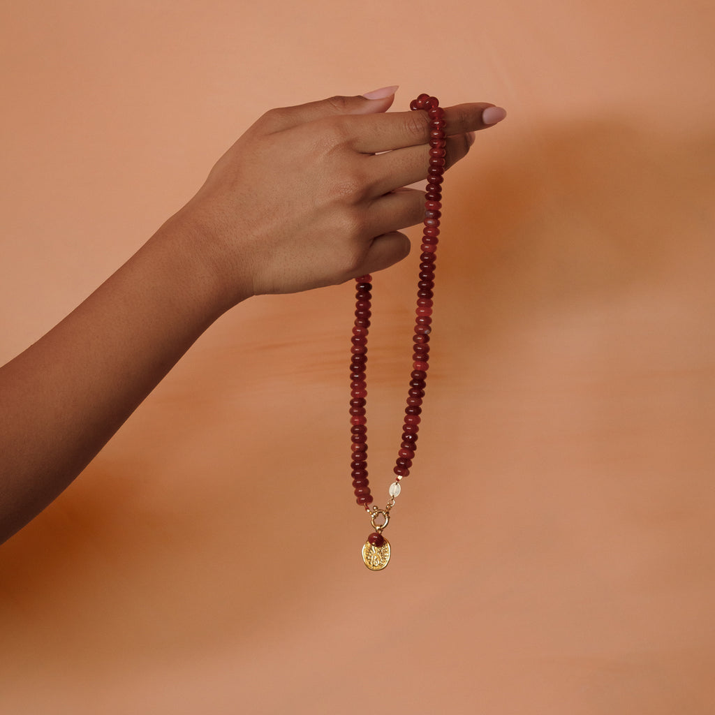 Hand holding the red agate beaded necklace with Zodiac coin pendant.