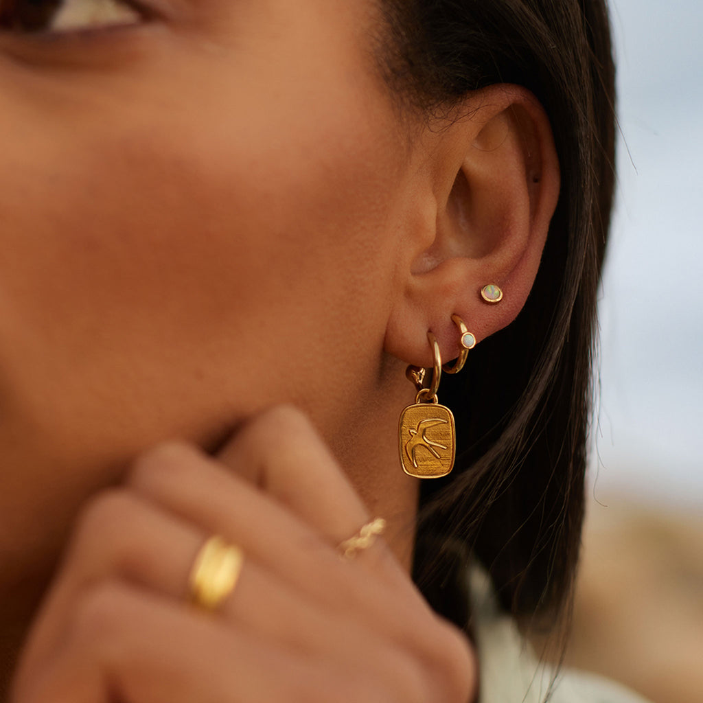 Gold charm earring with swallow hands from a gold hoop. Minimal, modern and understated jewellery. Designed and handcrafted in Devon. Mix and match to personalise your ear stack with Elemental single hoop earrings.