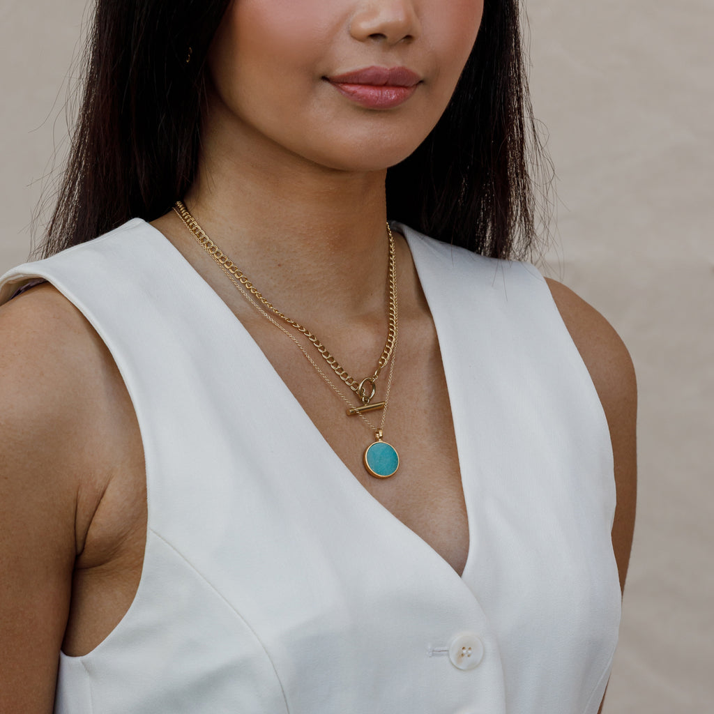 A slice of Amazonite is set in a circular brushed gold vermeil pendant. The turquoise toned pendant hangs on a minimal gold fill chain, styled with a yellow beaded choker necklace.