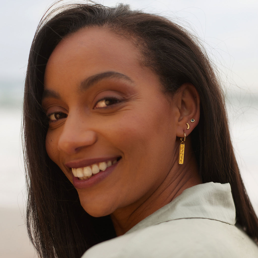 Vertical gold bar with the moons phases hangs from a gold hoop earring. Mix and match single Elemental charm hoop earrings to create your own unique ear stack. Styled with gold luna moon stud and gemstone stud earrings. Shop gold vermeil everyday, minimal jewellery at Wanderlust Life online.