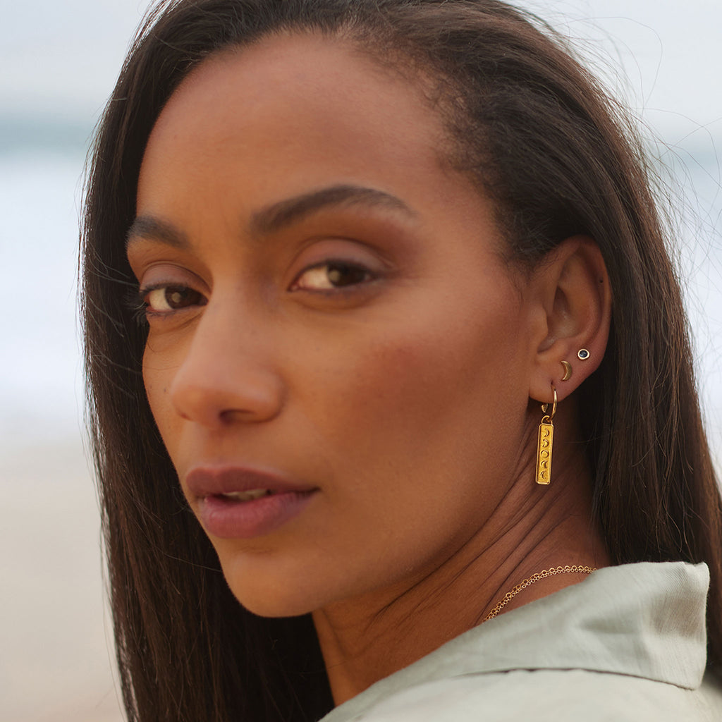 Vertical gold bar with the moons phases hangs from a gold hoop earring. Mix and match single Elemental charm hoop earrings to create your own unique ear stack. Styled with gold luna moon stud and gemstone stud earrings. Shop gold vermeil everyday, minimal jewellery at Wanderlust Life online.