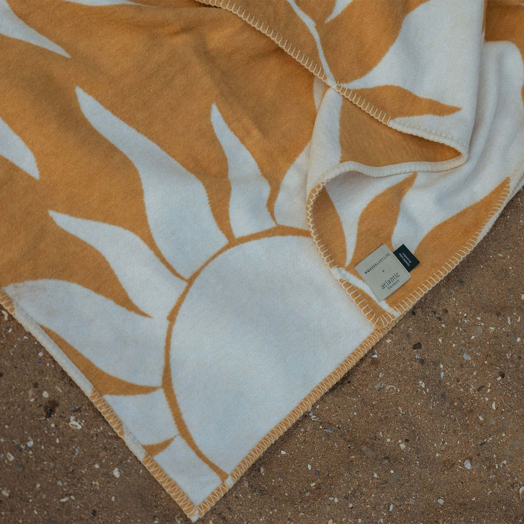 Created with recycled cotton, a reversible blanket featuring a sun motif with golden yellow tones. Designed by Wanderlust Life and Atlantic Blankets, made in the UK.