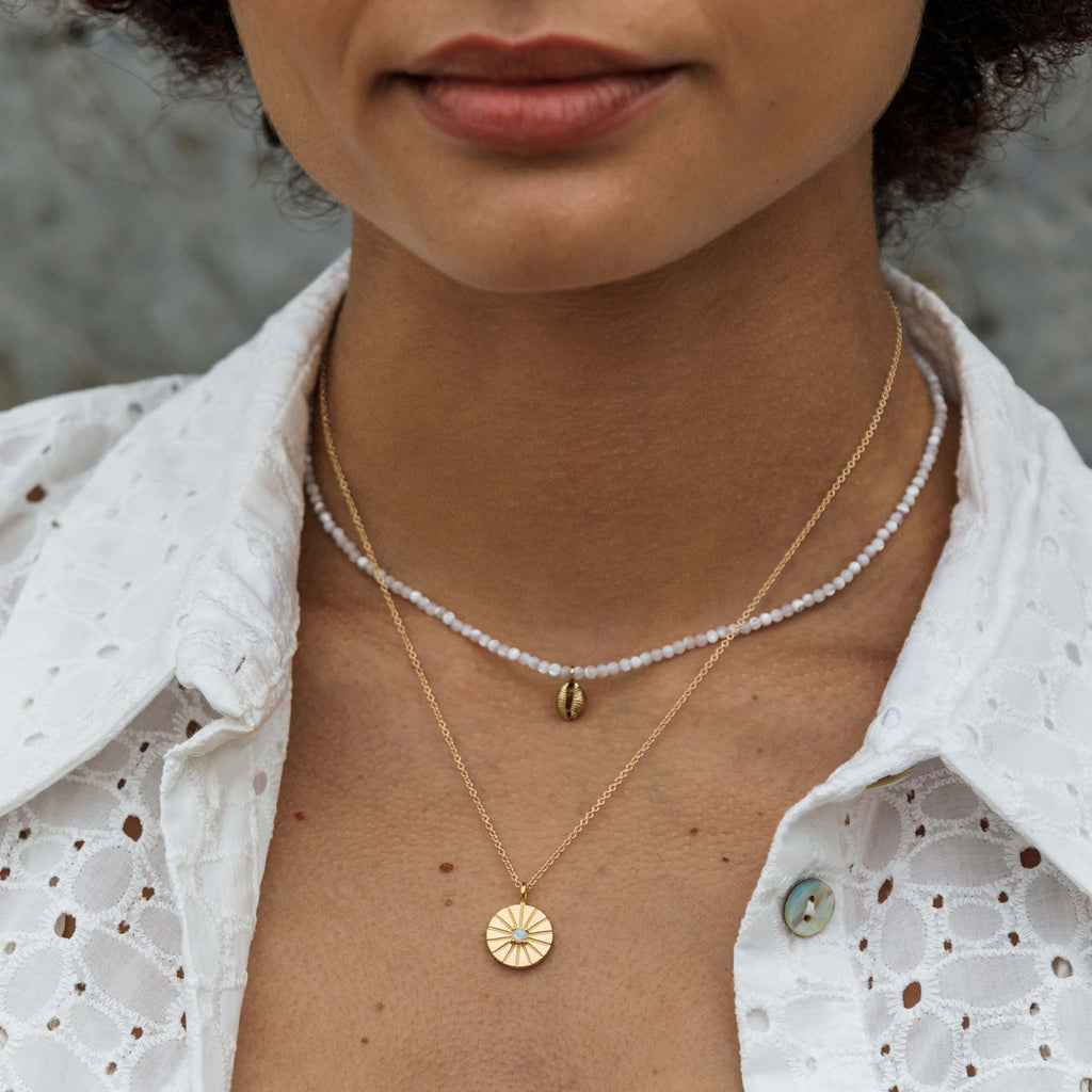 A dainty hand-cast cowry shell dances on a mother of pearl beaded choker necklace. Styled in a minimal necklace stack, layered with the Opal Mini Sundial Necklace.