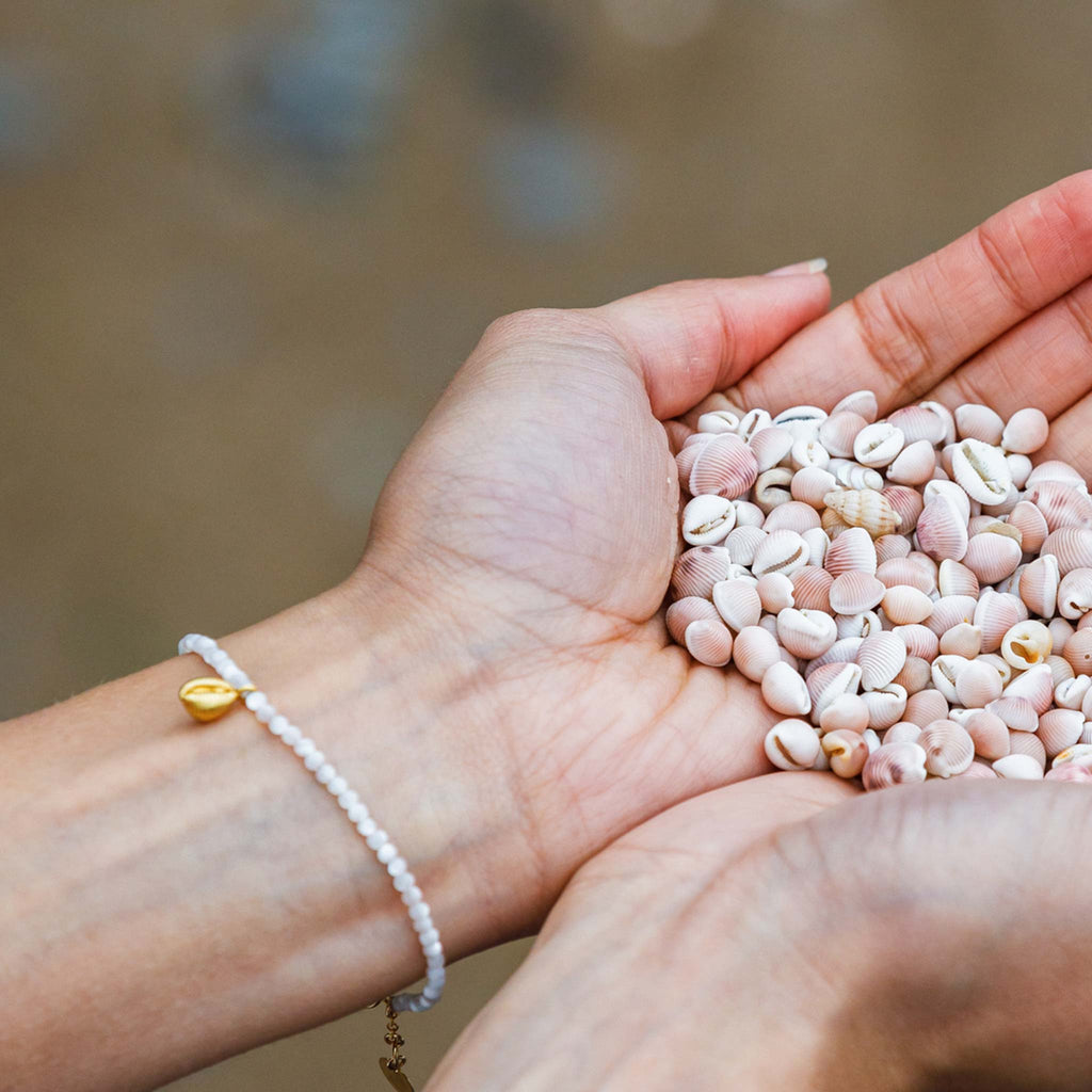 A mother of pearl beaded bracelet includes a dainty hand-cast cowry from our collection of seashells sourced from local beaches.