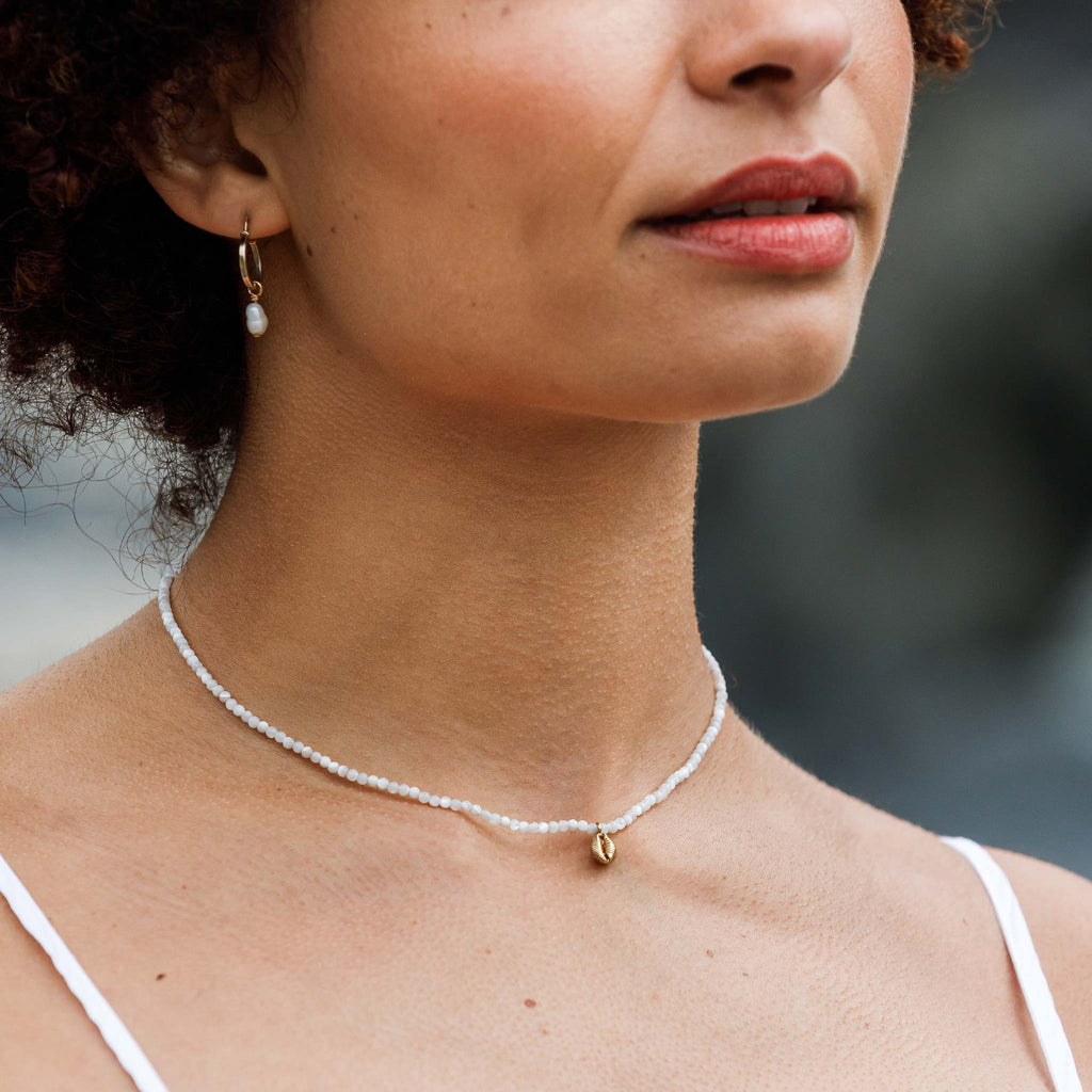 A dainty hand-cast cowry shell dances on a mother of pearl beaded choker necklace.