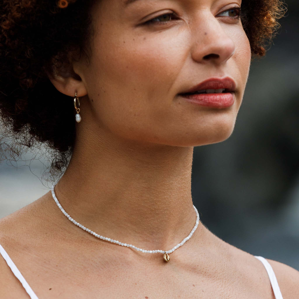 A dainty hand-cast cowry shell dances on a mother of pearl beaded choker necklace.
