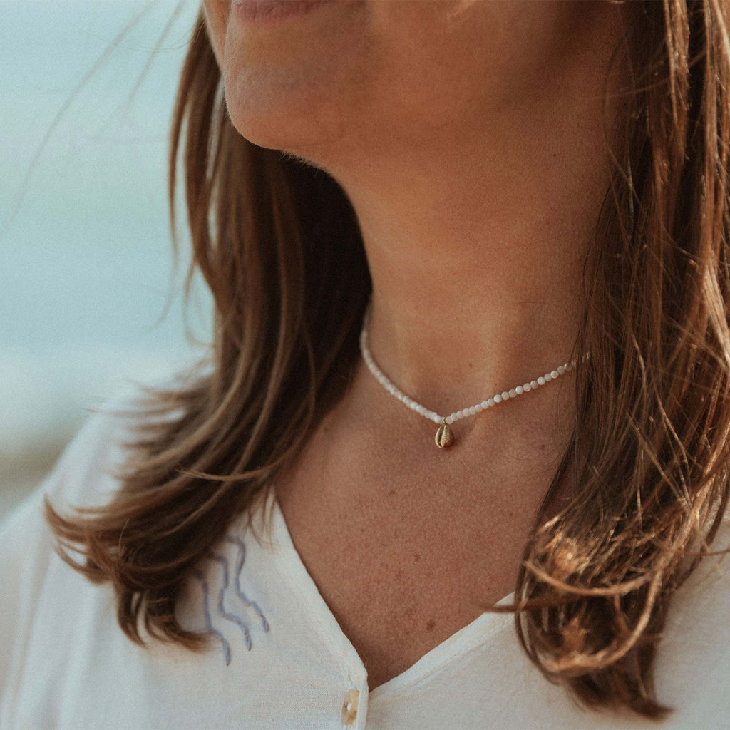 A dainty hand-cast cowry shell dances on a mother of pearl beaded choker necklace.