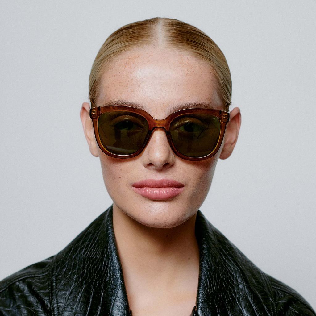 An oversized cat-eye style of sunglasses with brown frames and green lenses.