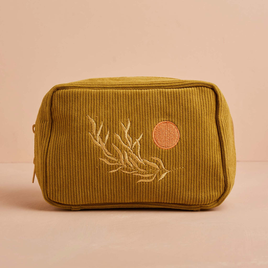 An olive coloured makeup bag, made with corduroy fabric and featuring an embroidered leaf and sun design. This bag features a zip closure and internal pockets, perfect for storying makeup.