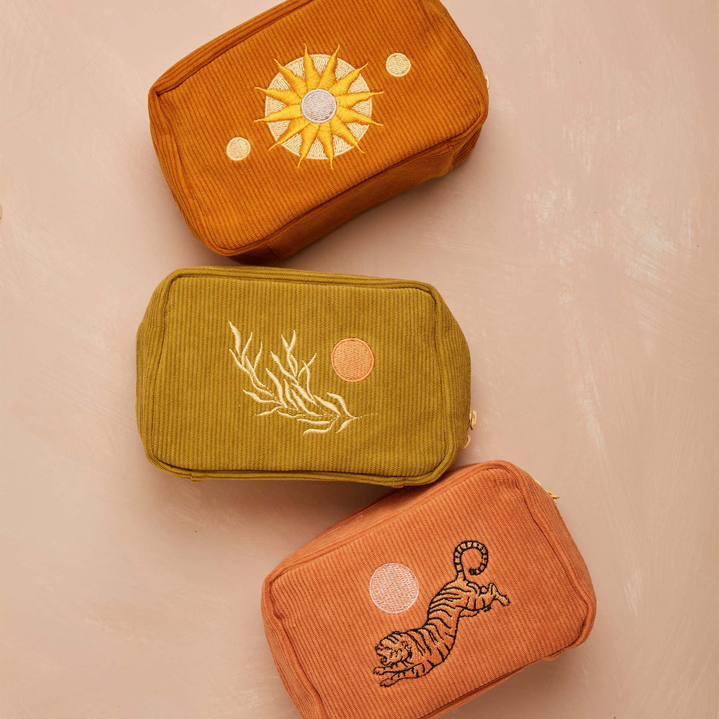 Three corduroy makeup bags by Cai and Jo, each feature a unique embroidered design - a sun, leaf, and tiger.