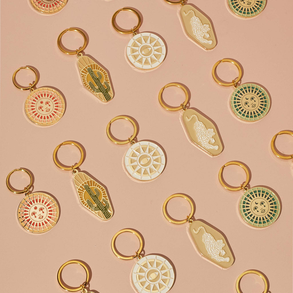 A gold plated motel key style key chain features a cactus and sun-ray design, made with soft enamel and gold plating.