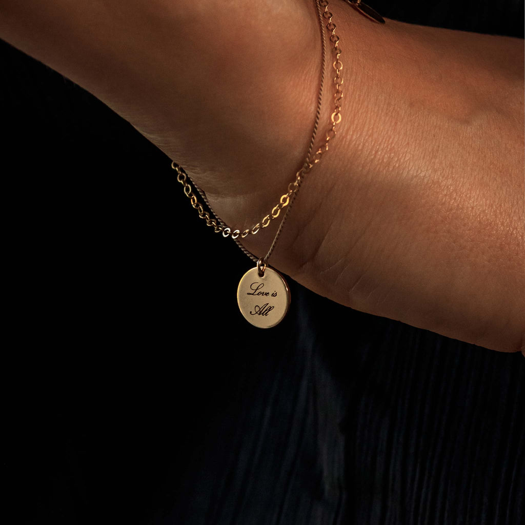 Charged with meaning, an engravable disc slides on a delicate bracelet of gold and silk. You can engrave on one or both sides with complimentary engraving.