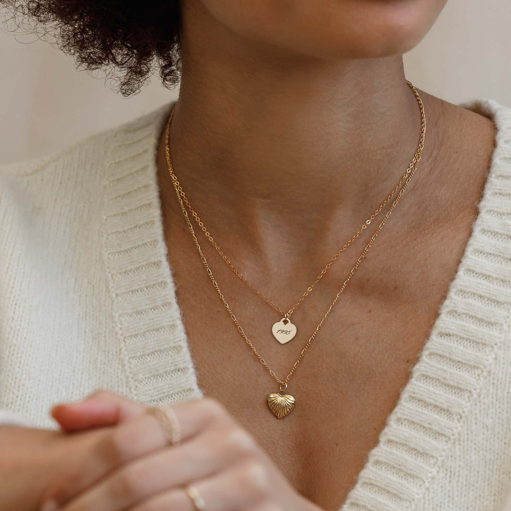 The Engraved Love Notes Necklace on a minimal gold fill chain is styled with the Valentino heart necklace on a minimal Figaro chain. This double heart necklace stack is meaningful yet minimal.