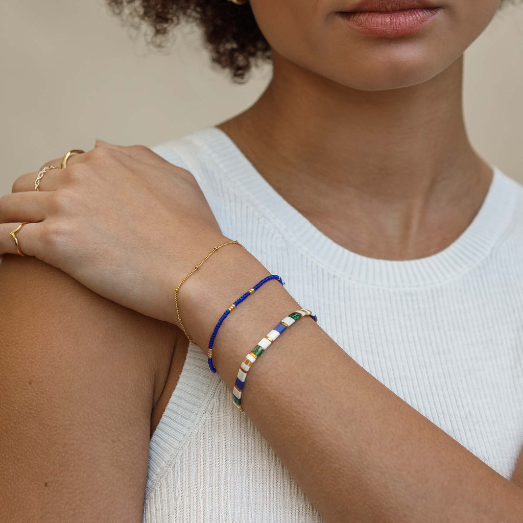 The Fez Layering Bracelet is a multicolour, cool tonal bracelet. Tila beads in white, blue, green and gold create an alternating pattern inspired by Moroccan tiles. Styled stacked with a minimal gold bracelet and another beaded bracelet.