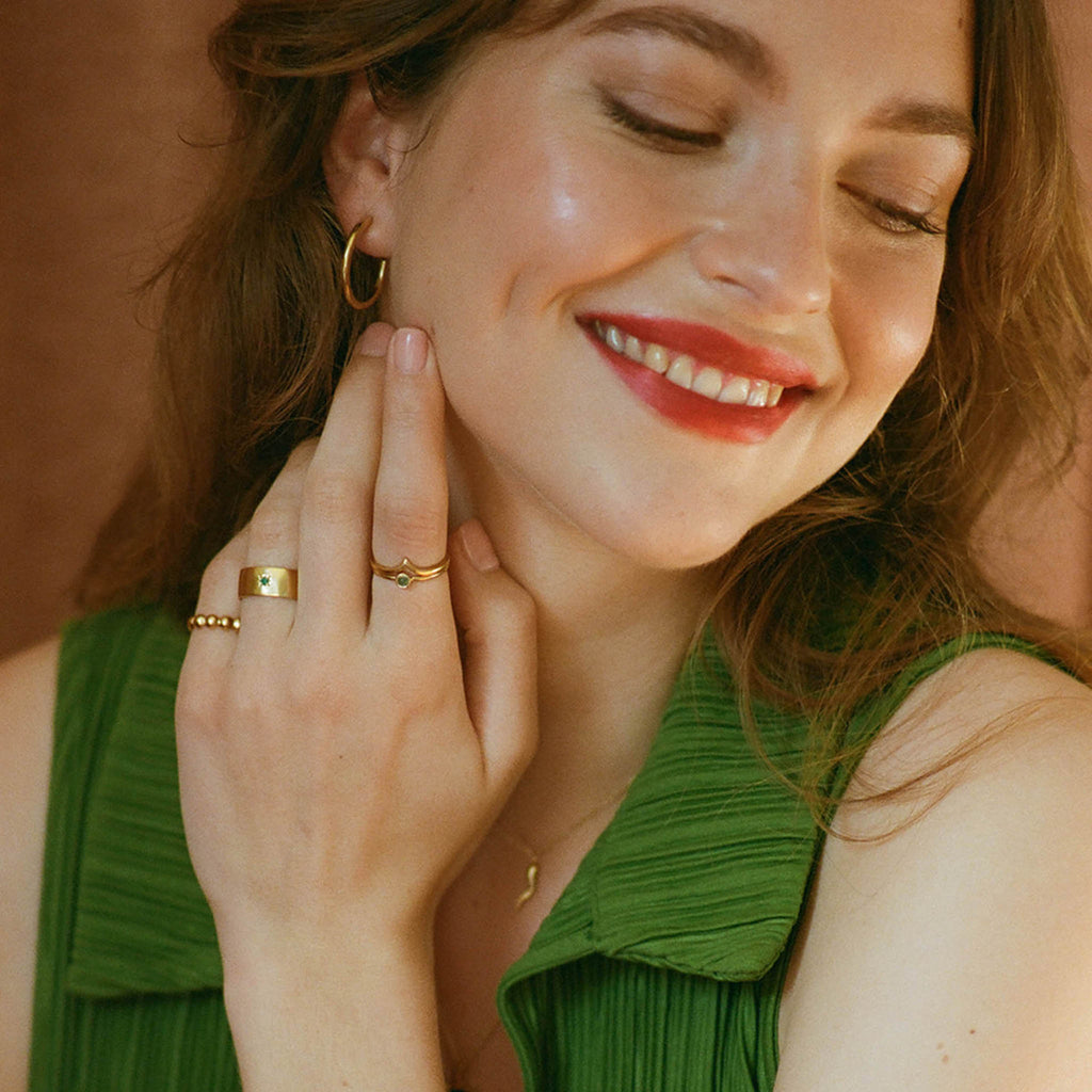 From the Revival SS22 collection, the Sigaro Ring features a star set green onyx gemstone, and is effortlessly styled into this ring stack. Model wears a wishbone ring and emerald ring stacked. Pictured with timeless, gold Silke hoop earrings.
