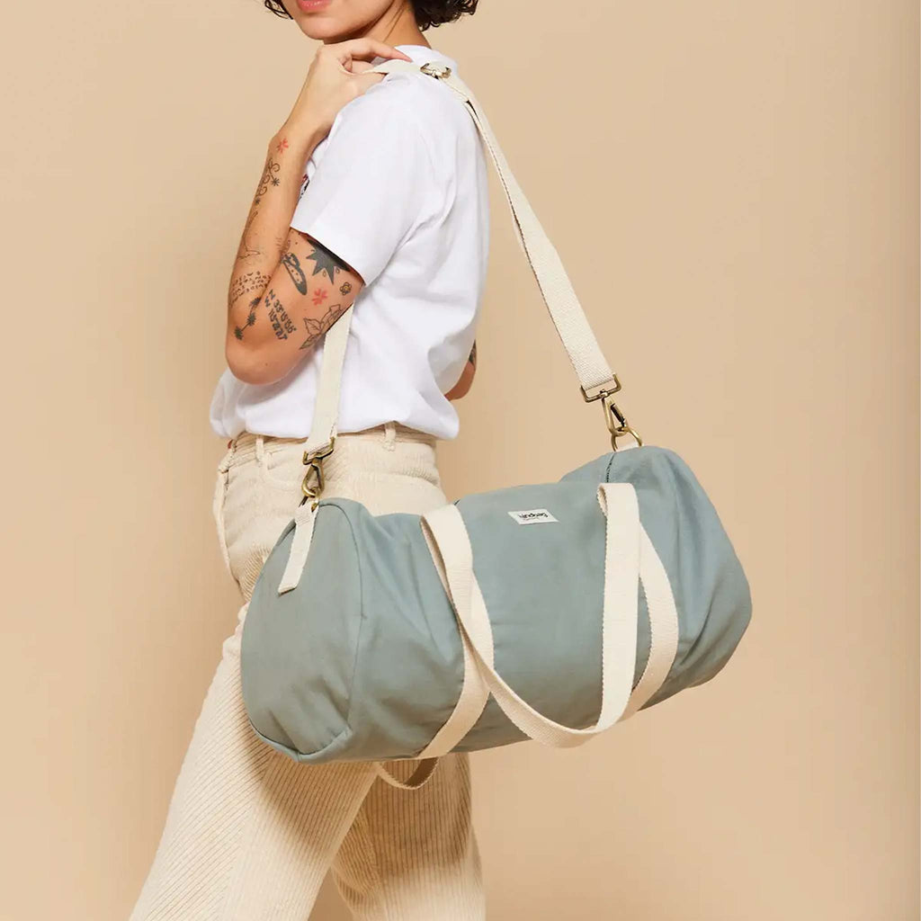 A rounded duffel bag in a shade of blue sage. Theres a detachable strap and two other straps in cream.