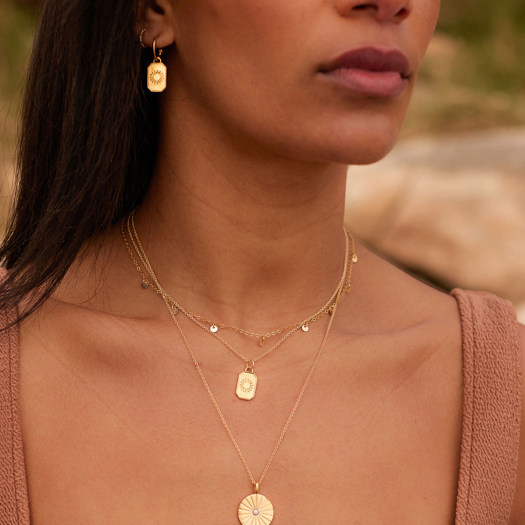 Ignis Pendant Necklace. A stylised sun is set in an octagonal gold pendant, suspended on a minimal gold chain necklace. Customise this engravable piece with a name or date with our complimentary engraving service. The perfect meaningful gift for fire signs, and an effortless layering essential. Sustainably handcrafted in the UK with recycled silver and gold vermeil. Designed in our Devon studio.