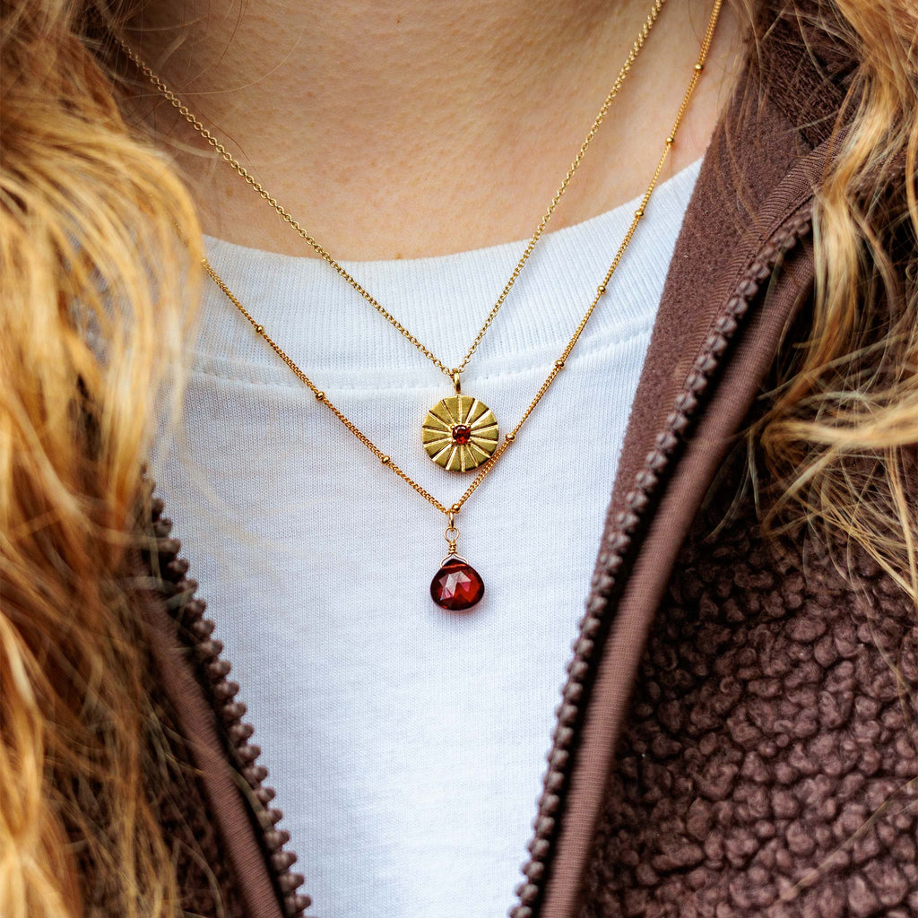 A meaningful, January birthstone necklace stack featuring the a faceted garnet gemstone on a Satellite Chain and the mini sundial pendant necklace. 