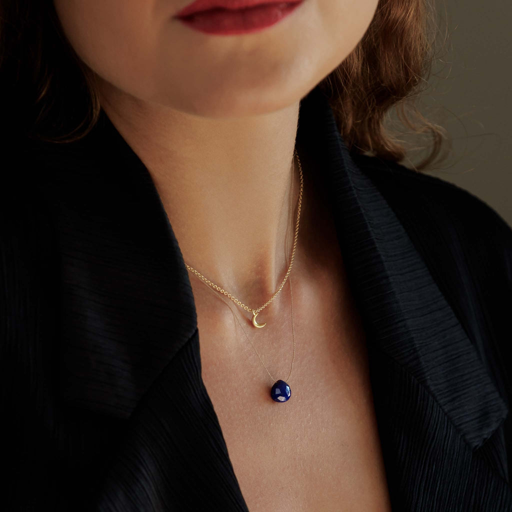 A Lapis Lazuli gemstone in a deep, navy blue with gold flecks is strung on a fine cord, creating a minimal and modern gemstone necklace. 