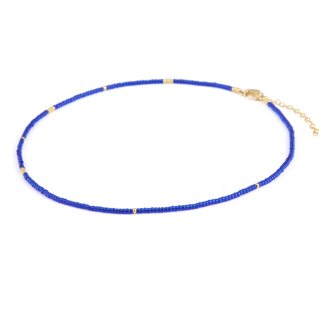 A blue beaded necklace features small bright cobalt blue beads all the way around, contrasted at intervals with gold beads. This necklace features an adjustable length. Designed and handcrafted in our Devon studio.
